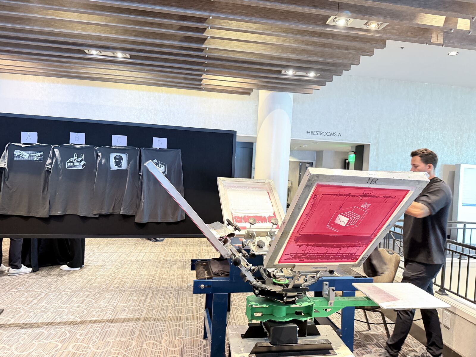 Screen printing demonstration with an operator running the press while guests watch