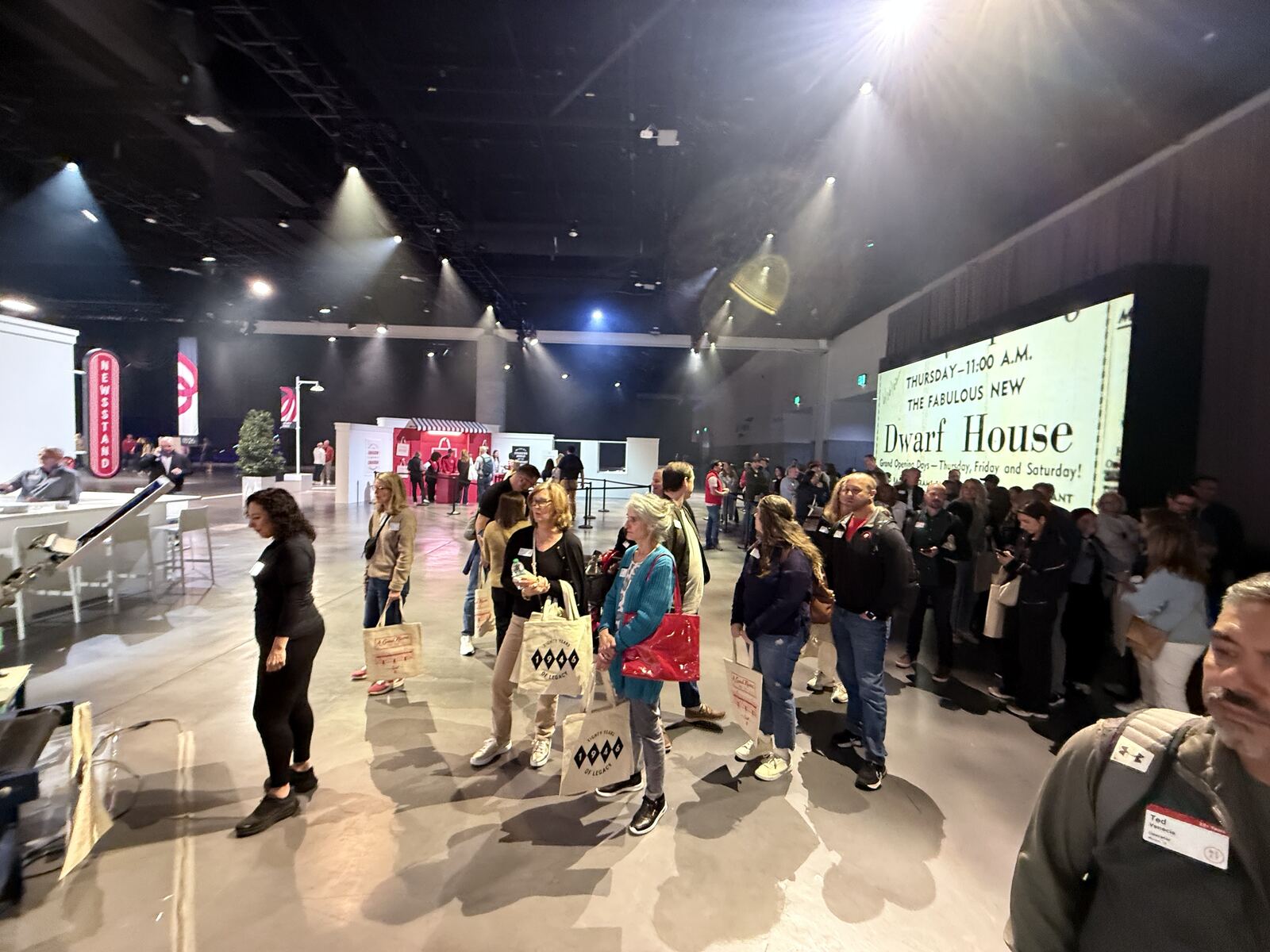 Wide venue shot of a crowded event space with a stage and multiple branded booths